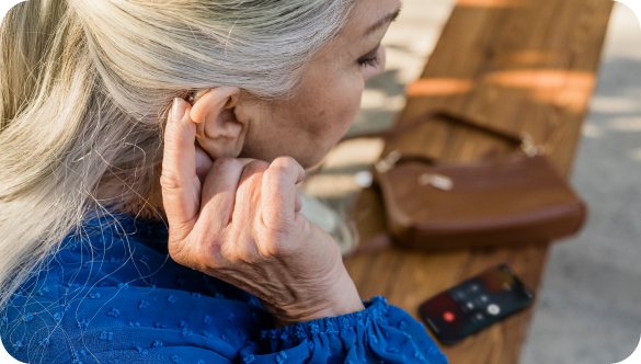 An older woman adjusts her behind-the-ear hearing aid on her right ear.